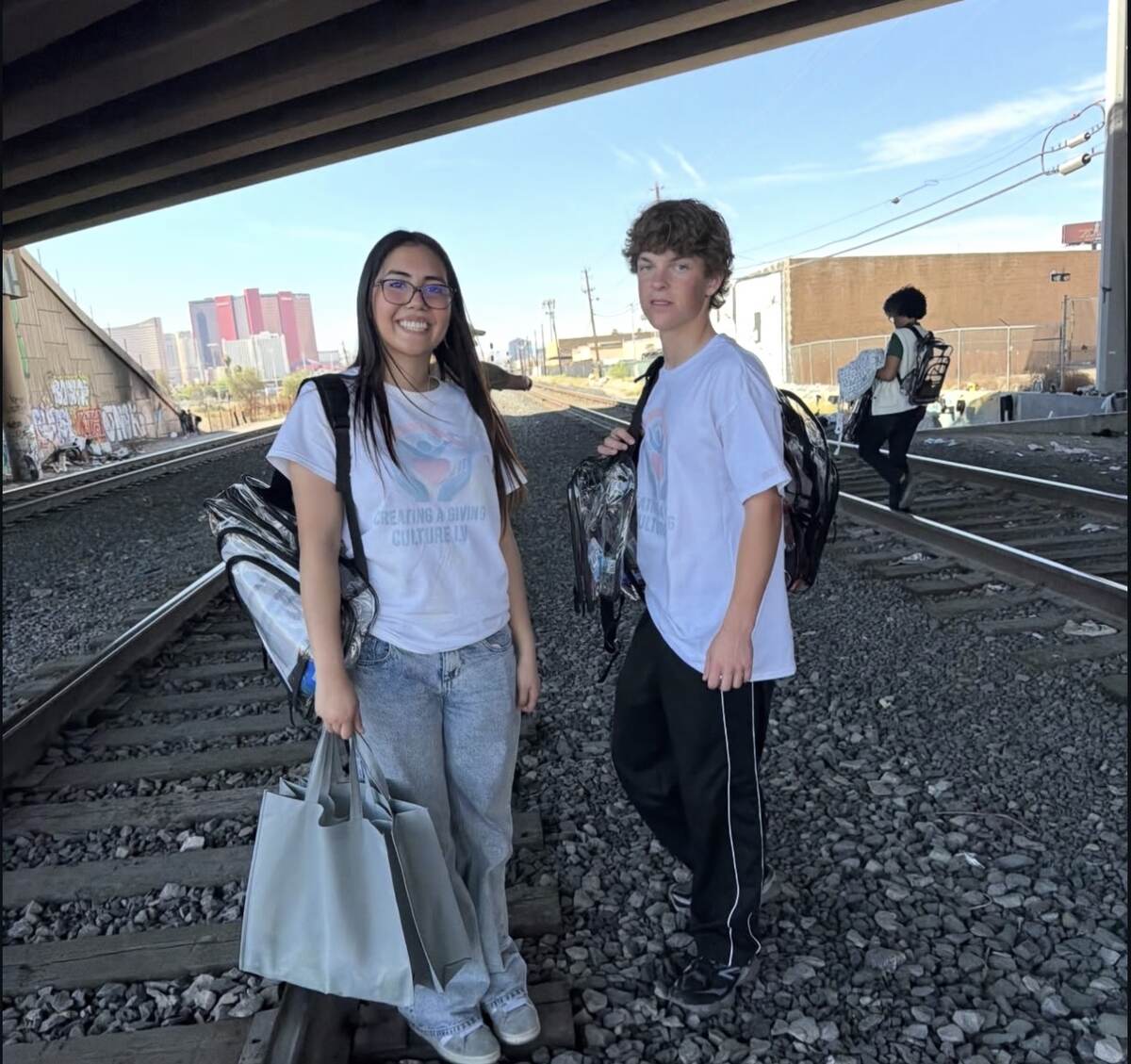 Young volunteers carrying backpacks beneath a downtown overpass