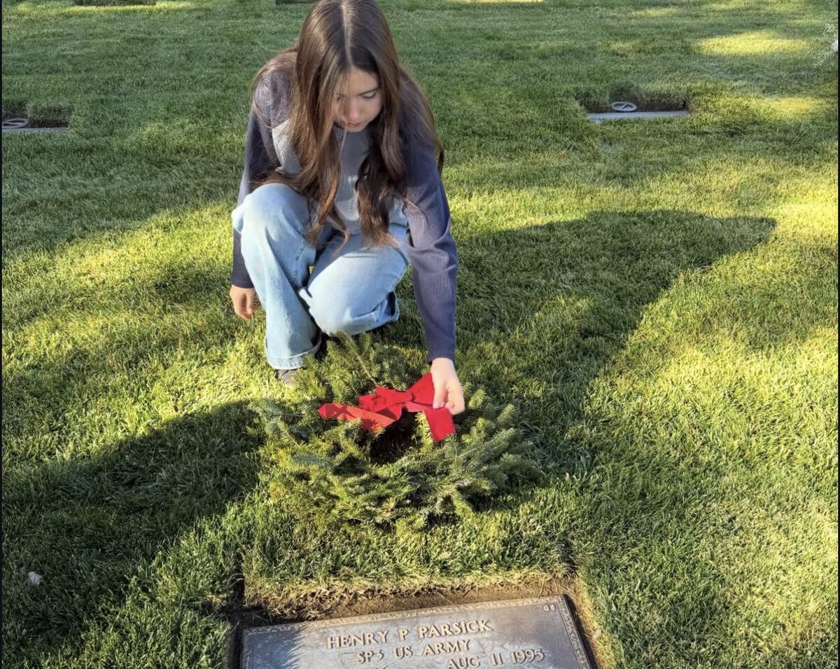 Young volunteer carefully placing a wreath on a veteran's grave
