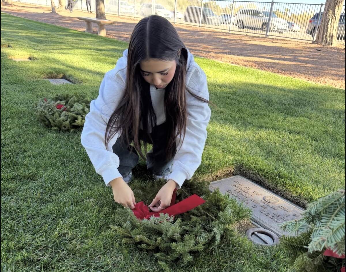 Aiyana securing the red bow on a veteran's memorial wreath